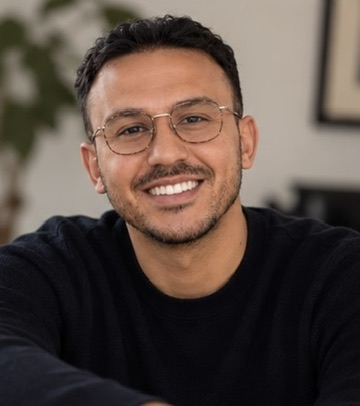 Saad Benryane smiling, wearing glasses and a black sweater.